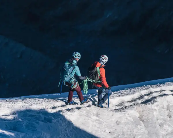 Dwóch alpinistów z rakami i czekanami wspina się po ośnieżonym zboczu.