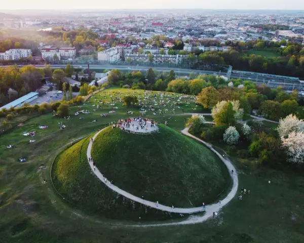 Kraków nietypowe atrakcje: Kopiec Krakusa z ludźmi na szczycie i piknikującymi na trawie. W tle rozciąga się panorama miasta.