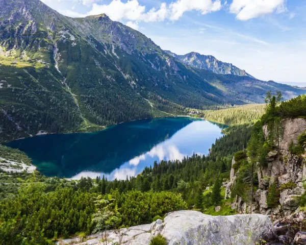 Widok na Morskie Oko, perłę polskich gór Tatr. Lśniąca tafla jeziora odbija błękitne niebo i otaczające je szczyty.