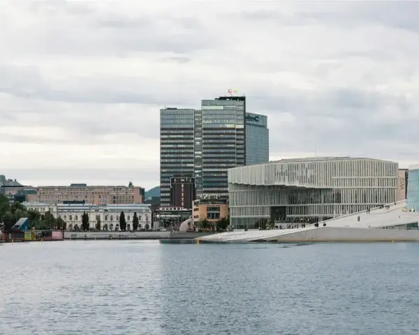 Nowoczesna architektura nad wodą, idealne miejsce, by zobaczyć, co robic w Oslo. W tle wysokie budynki i zabytkowe kamienice.