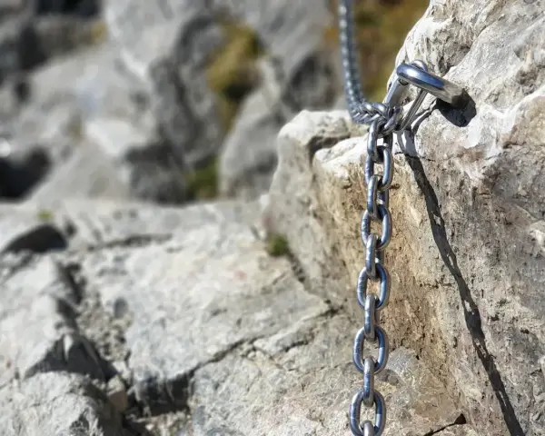 Łańcuch ułatwiający wejście na Giewont, przytwierdzony do skalnej ściany. Widok na kamienisty szlak.