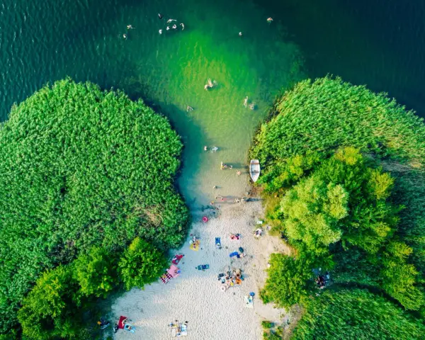 Letnie orzeźwienie nad jednym z najpiękniejszych jezior na południu Polski. Ludzie kąpią się, plażują, a łódka czeka przy brzegu.