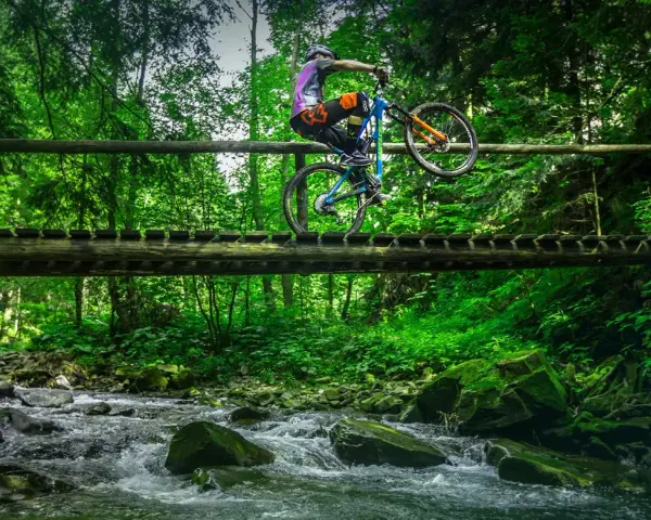 Rowerzysta wykonuje trik na drewnianym moście nad górskim potokiem. Niesamowite trasy rowerowe Zakopane czekają na odkrycie!