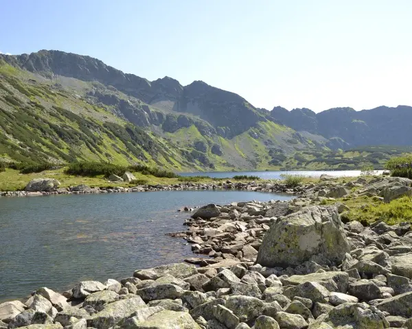 Malownicze jezioro w Tatrach, idealne na szlaki turystyczne Zakopane. Kamieniste brzegi i zielone zbocza gór tworzą piękny krajobraz.