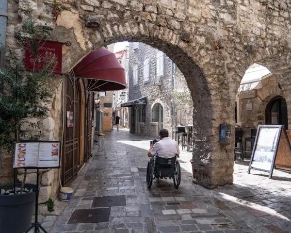 Mężczyzna na wózku inwalidzkim przemierza urokliwe uliczki budva stare miasto, podziwiając kamienne łuki i zabytkową architekturę.