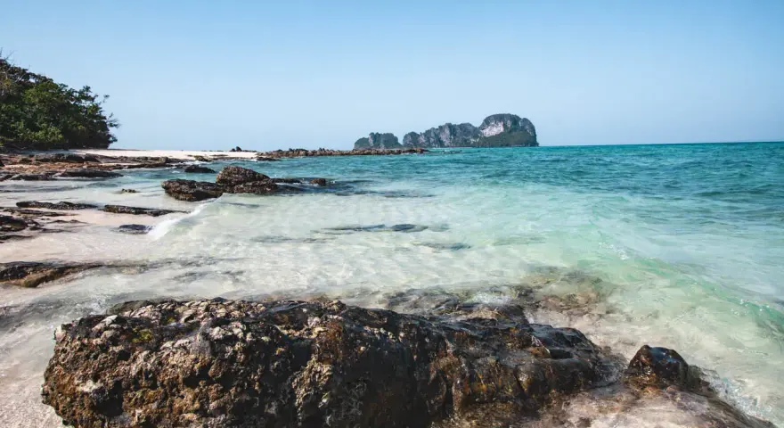 Piękne plaże i turkusowa woda, idealne miejsca w Krabi, co zobaczyć. Skały i zieleń na tle błękitnego nieba.