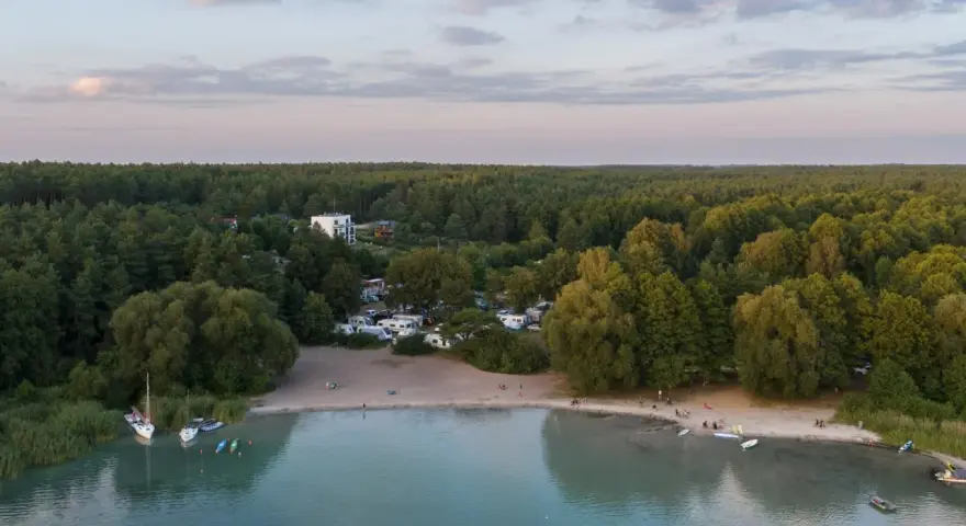 Plaża nad najczystszym jeziorem w Polsce. Woda jest turkusowa, a na brzegu widać łodzie, kajaki i ludzi odpoczywających na piasku.