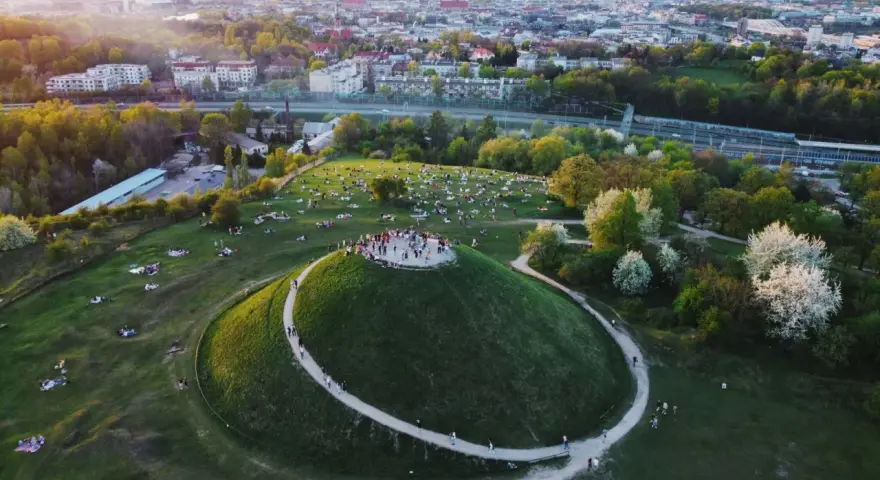 Kraków nietypowe atrakcje: Kopiec Krakusa z ludźmi na szczycie i piknikującymi na trawie. W tle rozciąga się panorama miasta.