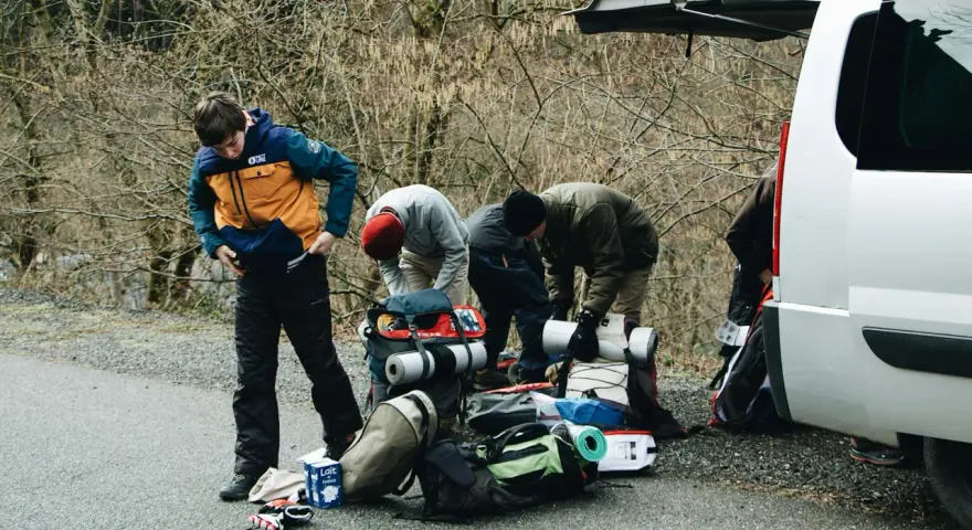 Przygotowania do wyprawy w **Tatry w Polsce**. Grupa ludzi pakuje sprzęt turystyczny przy otwartym bagażniku białego vana.