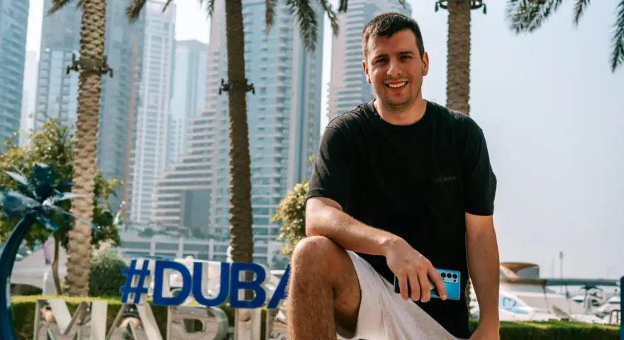 Uśmiechnięty mężczyzna z telefonem w dłoni na tle Dubaju. #Dubaj co warto wiedzieć, to świetny kierunek na wakacje.
