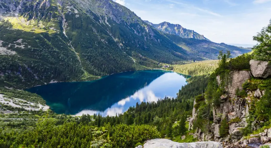 Widok na Morskie Oko, perłę polskich gór Tatr. Lśniąca tafla jeziora odbija błękitne niebo i otaczające je szczyty.