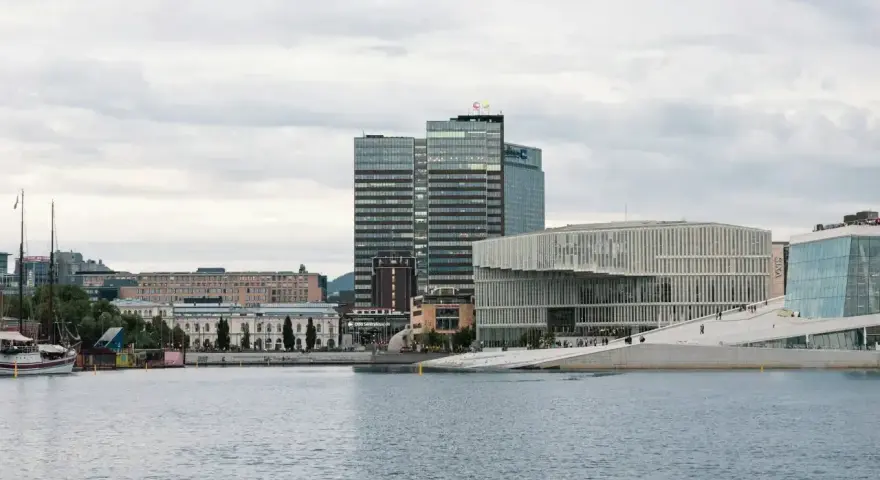 Nowoczesna architektura nad wodą, idealne miejsce, by zobaczyć, co robic w Oslo. W tle wysokie budynki i zabytkowe kamienice.