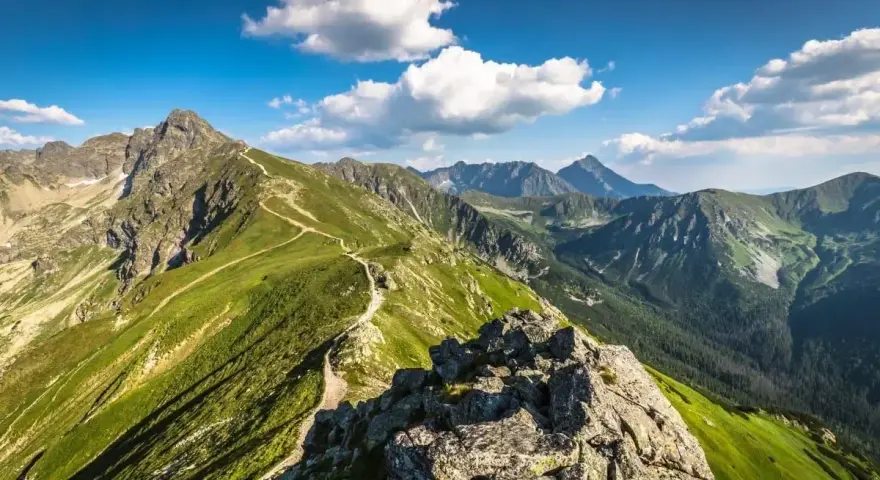Widok na szlak prowadzący na Kasprowy Wierch. Zielone zbocza, skaliste szczyty i błękitne niebo z chmurami.