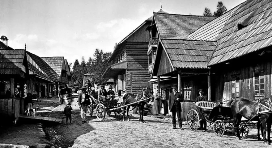 Ulica Kościeliska w Zakopanem, z drewnianymi domami i ludźmi w tradycyjnych strojach, powozy konne.