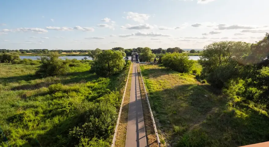Słoneczna ścieżka rowerowa w zachodniopomorskim prowadzi przez zielone tereny nad rzeką, zachęcając do aktywnego wypoczynku.