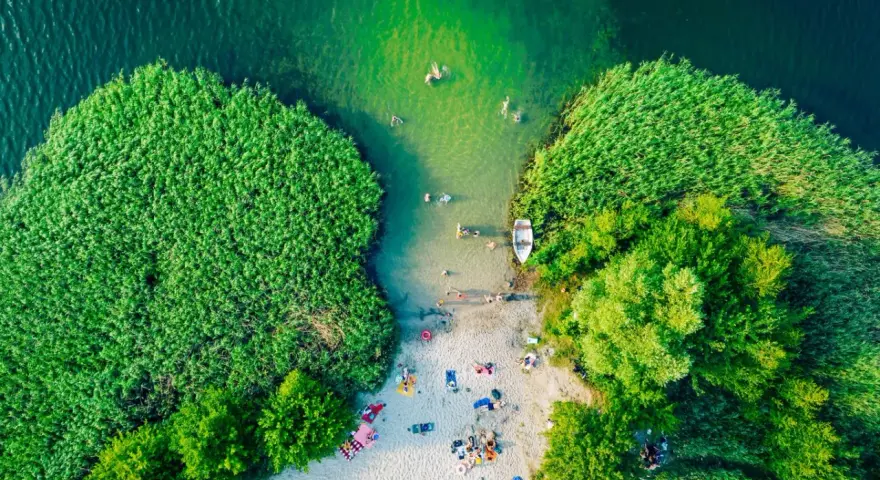 Letnie orzeźwienie nad jednym z najpiękniejszych jezior na południu Polski. Ludzie kąpią się, plażują, a łódka czeka przy brzegu.