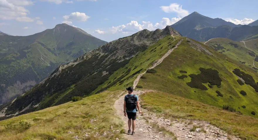 Szlak na Ornaka z Doliny Kościeliskiej. Turysta z plecakiem idzie kamienistą ścieżką pośród zielonych zboczy Tatr.