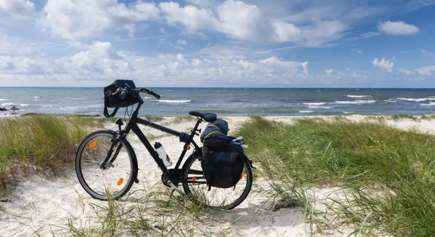 Rower z sakwami gotowy na przygodę. Trasa rowerowa wzdłuż Bałtyku zapowiada się wspaniale, z piaszczystą plażą i szumem fal.