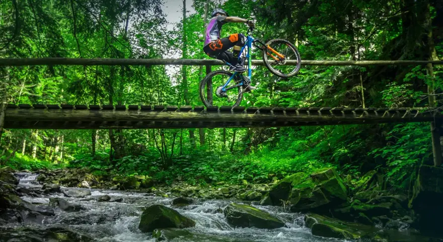Rowerzysta wykonuje trik na drewnianym moście nad górskim potokiem. Niesamowite trasy rowerowe Zakopane czekają na odkrycie!