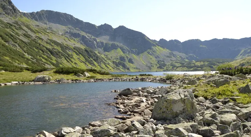 Malownicze jezioro w Tatrach, idealne na szlaki turystyczne Zakopane. Kamieniste brzegi i zielone zbocza gór tworzą piękny krajobraz.