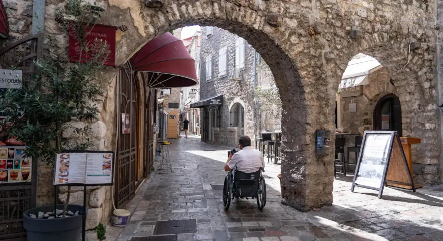 Mężczyzna na wózku inwalidzkim przemierza urokliwe uliczki budva stare miasto, podziwiając kamienne łuki i zabytkową architekturę.