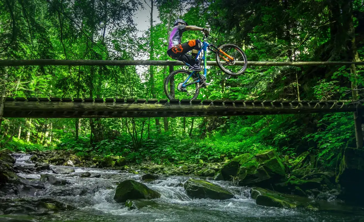 Rowerzysta wykonuje trik na drewnianym moście nad g&oacute;rskim potokiem. Niesamowite trasy rowerowe Zakopane czekają na odkrycie!