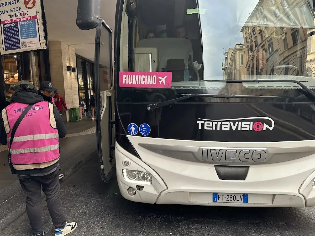 Autobus Terravision na lotnisko Fiumicino. Jak dojechać do centrum Rzymu? Pracownik w kamizelce kieruje pasażer&oacute;w.