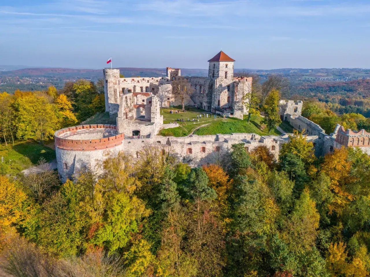 Ruiny zamku na Szlaku Orlich Gniazd pieszo, otoczone jesiennymi drzewami.