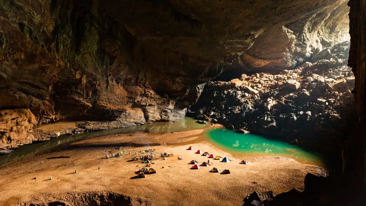 Ob&oacute;z w jaskini Hang Son Doong. Namioty rozbite na piaszczystej plaży nad turkusową wodą.