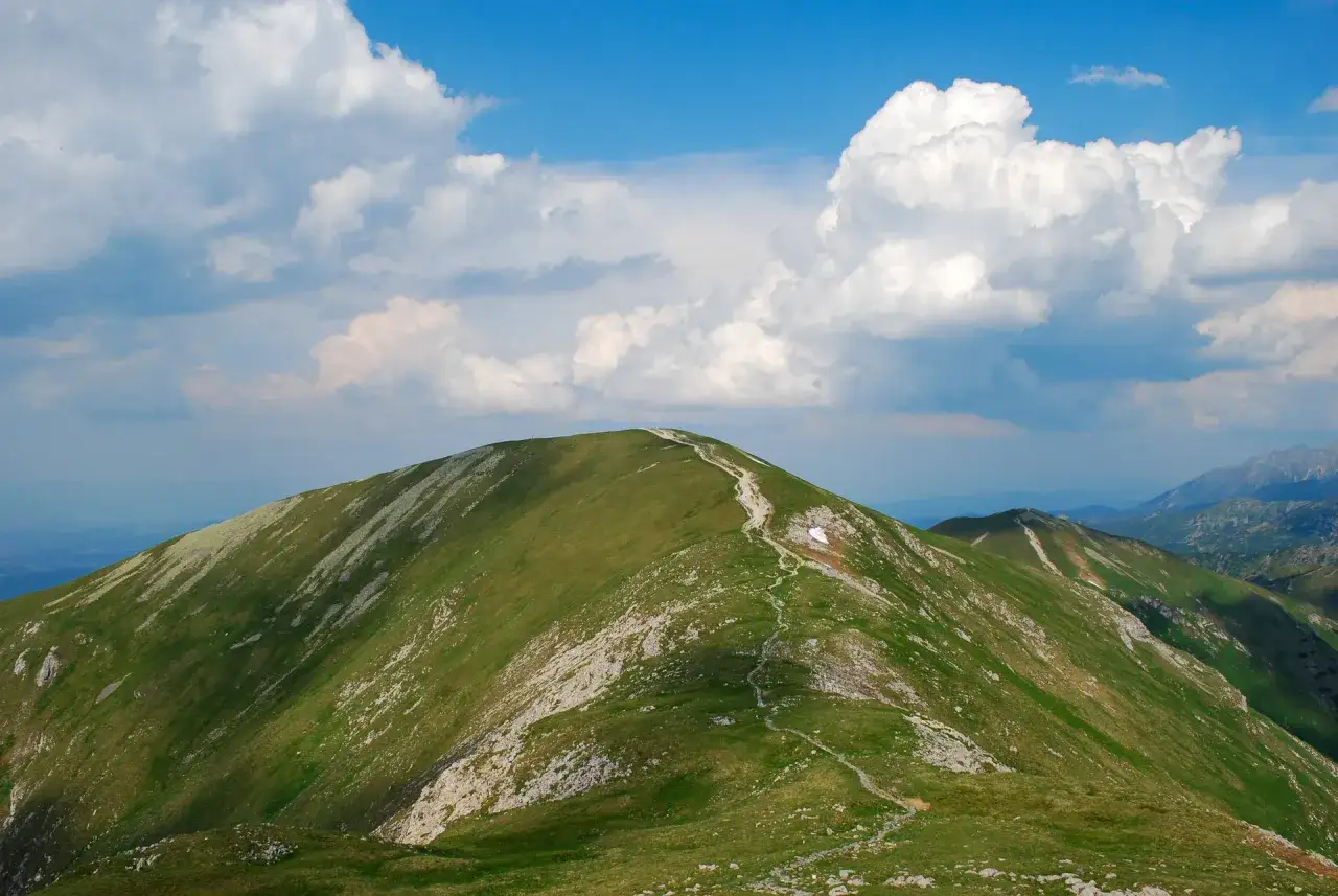 Wędrówka szlakiem na Czerwone Wierchy. Kręta ścieżka wije się po zielonych zboczach gór, pod błękitnym niebem z białymi chmurami.