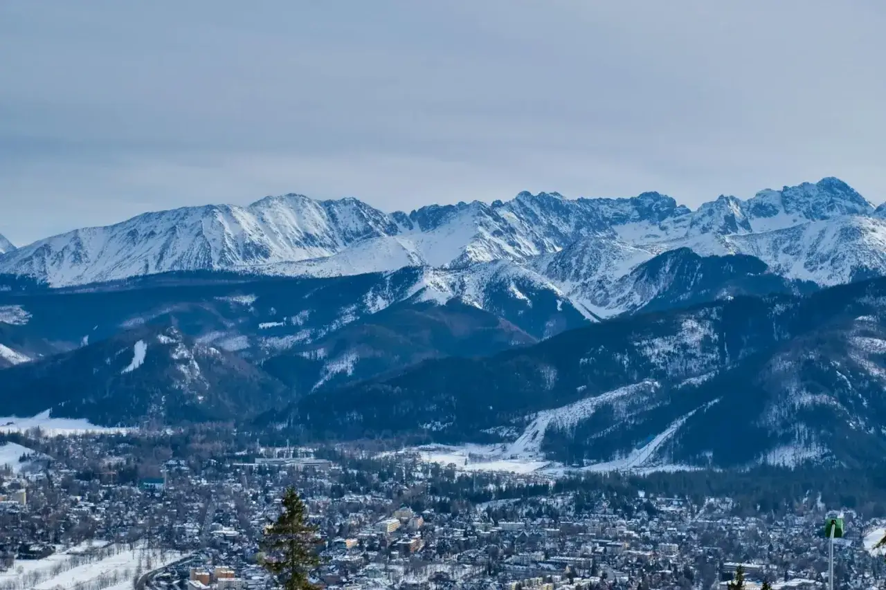 Zimowy krajobraz Tatr z ośnieżonymi szczytami i miasteczkiem u podn&oacute;ża. Idealne miejsce na wyjazd w Tatry zimą dla średniozaawansowanych.