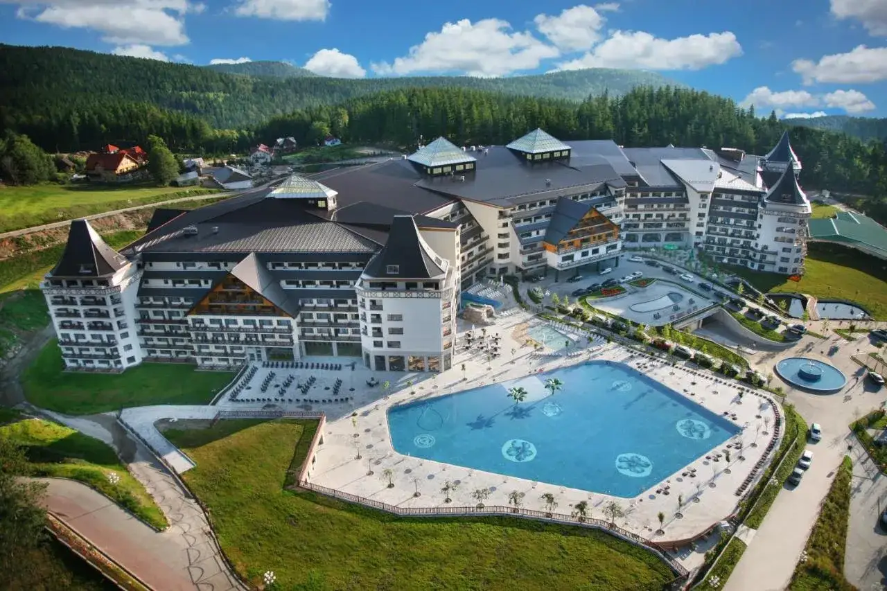 Imponujący hotel z basenami termalnymi, otoczony zielonymi wzgórzami i lasem.