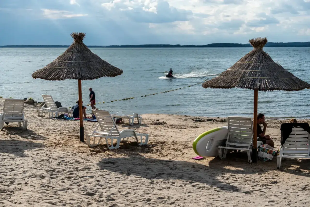 Plaża nad najczystszym jeziorem w Polsce. Leżaki, parasole i wodny skuter na horyzoncie.