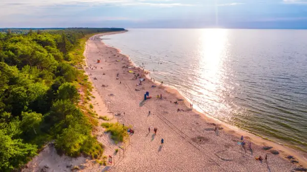 Piękna plaża nad Bałtykiem, idealna na fajne i tanie miejsca na wakacje w Polsce. Słońce odbija się w wodzie, a las tworzy malownicze tło.