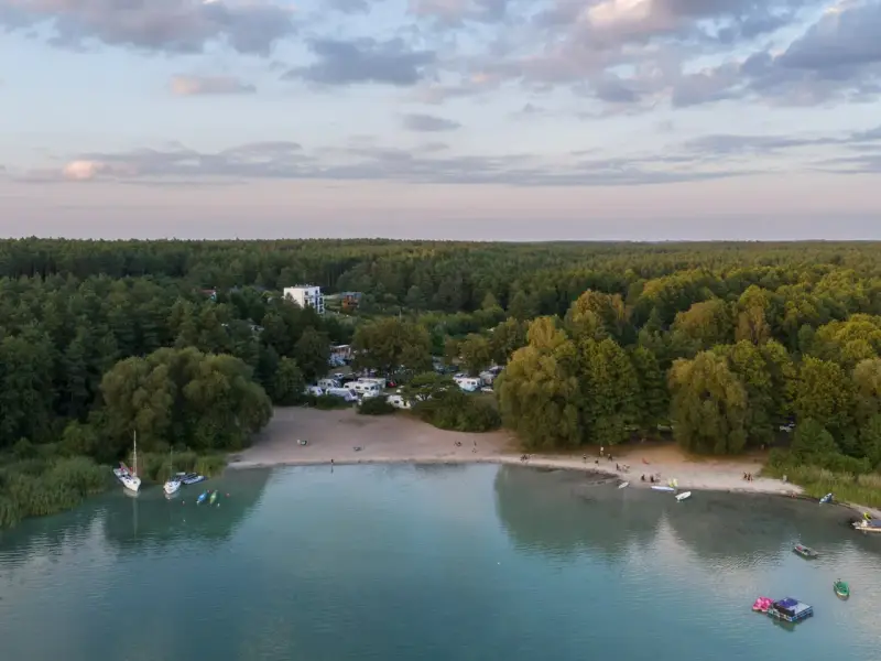 Plaża nad najczystszym jeziorem w Polsce. Woda jest turkusowa, a na brzegu widać łodzie, kajaki i ludzi odpoczywających na piasku.
