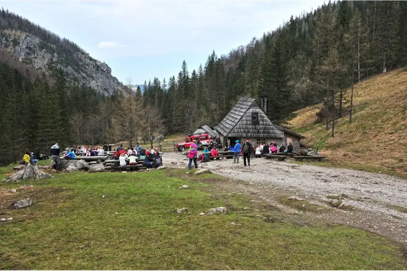 Ludzie odpoczywają przy bacówce na trasie Dolina Strążyska. W tle las i góry.